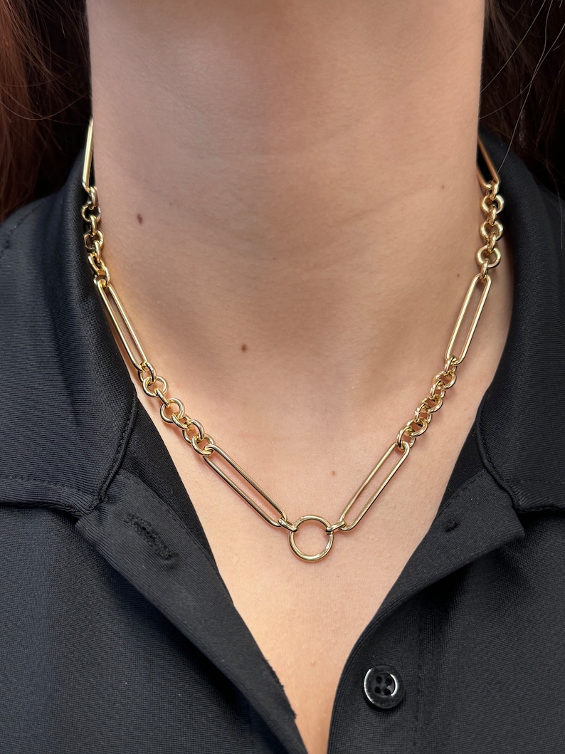 May include: A gold chain necklace with a large, round, open circle pendant.