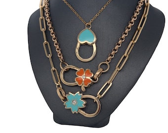 Puede incluir: Un collar de oro de varias capas con tres colgantes. Los colgantes son un corazón turquesa, una flor turquesa y una flor naranja. El collar está en un expositor gris.