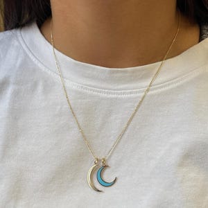 K&ouml;nnte beinhalten: Eine goldene Kettenkette mit zwei Halbmondanh&auml;ngern. Die Monde sind in Gold umrandet und mit hellblauem Email gef&uuml;llt.