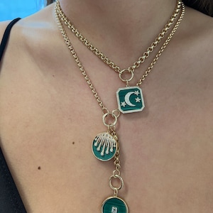 May include: A gold chain necklace with three green and gold pendants. The largest pendant features a crescent moon and stars, the middle pendant has a cluster of diamonds, and the smallest pendant has a single diamond.