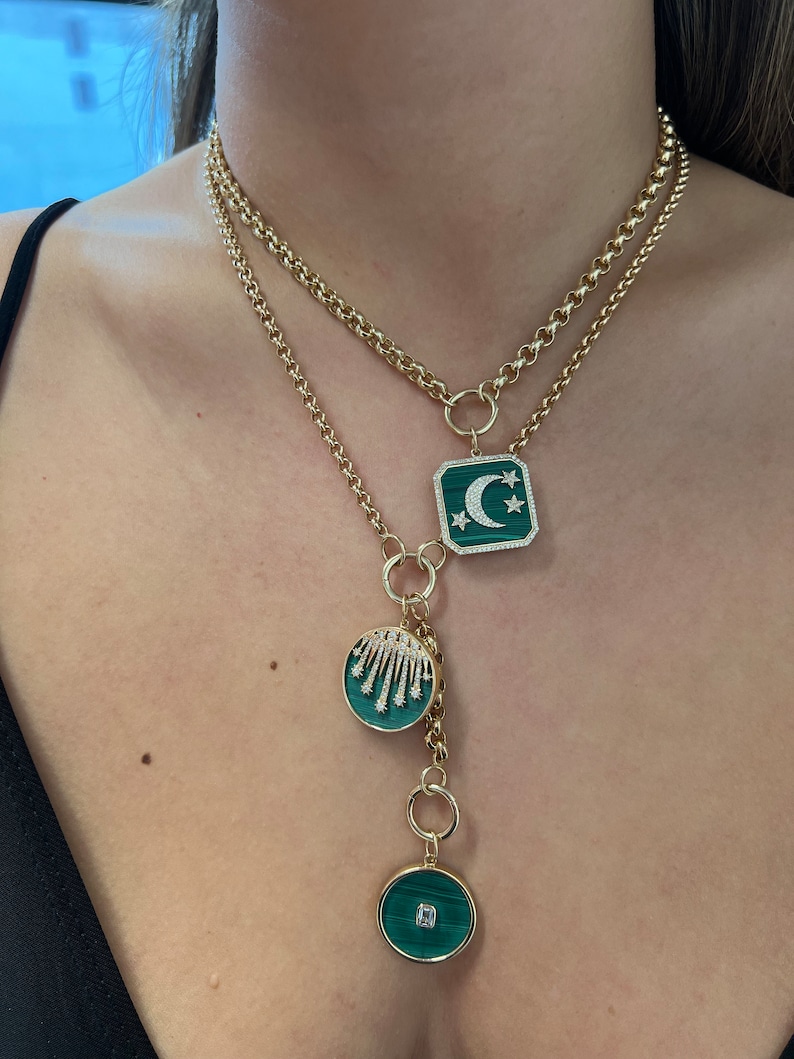 May include: A gold chain necklace with three green and gold pendants. The largest pendant features a crescent moon and stars, the middle pendant has a cluster of diamonds, and the smallest pendant has a single diamond.