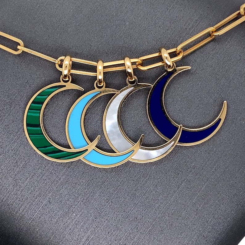 May include: A gold chain necklace with four crescent moon charms. Each charm is made of gold and has a different colored enamel inlay: green, blue, white, and dark blue.