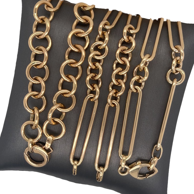 May include: A set of six gold chain necklaces of varying widths and styles, displayed on a gray velvet cushion.