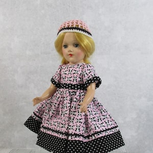 May include: A vintage doll wearing a pink dress with a panda pattern, black trim, and a black and white polka dot hem. The doll also wears a pink crocheted hat with a white and black trim.