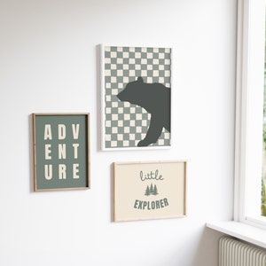 Könnte beinhalten: Drei gerahmte Drucke mit Waldmotiv. Der erste Druck zeigt eine schwarze Bärensilhouette auf einem grün-weiß karierten Hintergrund. Der zweite Druck sagt "ADVENTURE" in weißer Schrift auf grünem Hintergrund. Der dritte Druck sagt "little EXPLORER" in weißer Schrift auf beigefarbenem Hintergrund mit einer grünen Baumgrafik.