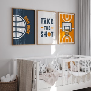 May include: Three framed prints with basketball themes. The first print is blue with a basketball and the text "Slam Dunk". The second print is white with the text "Take the Shot" and a basketball. The third print is orange with a basketball court and a basketball hoop.