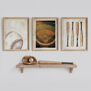 May include: Three framed wall art prints featuring a baseball, a baseball field, and four wooden bats. Below the frames, a wooden shelf holds a leather baseball glove containing a baseball and a single wooden baseball bat resting horizontally.