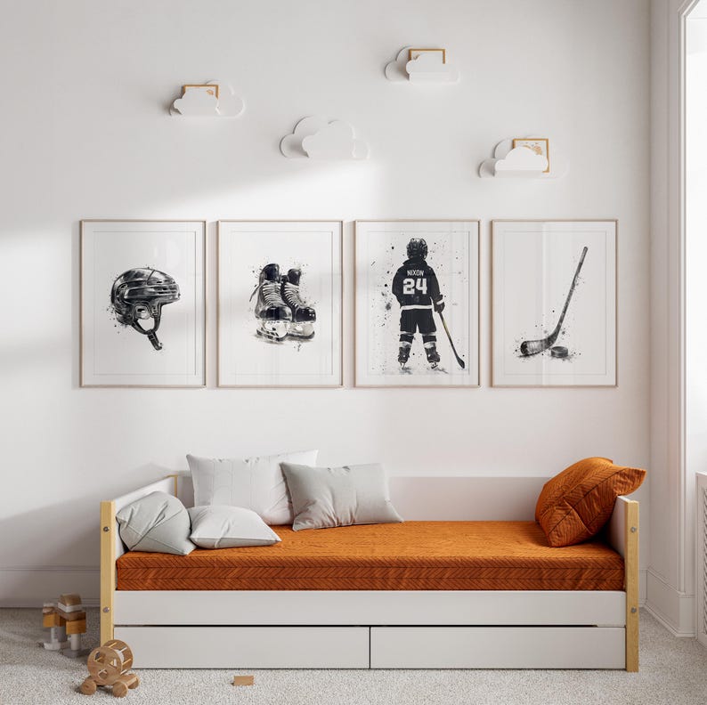 Pode incluir: Quatro quadros de parede com ilustra&ccedil;&otilde;es em aguarela a preto e branco de equipamento de h&oacute;quei no gelo, incluindo um capacete, patins, um jogador com o n&uacute;mero 24 e um stick de h&oacute;quei com um disco, expostos acima de um div&atilde;.