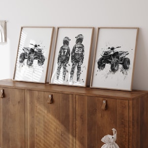 May include: Three framed wall art prints in light wood frames. The left and right prints feature black and white watercolor-style illustrations of ATVs. The center print shows two individuals in motocross gear with the numbers 17 and 22.