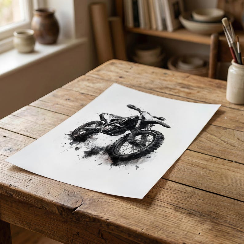 May include: A black and white ink wash illustration of a dirt bike printed on a rectangular piece of white paper. The artwork features a detailed motorcycle with knobby tires and a frame, rendered with expressive splatters and dark ink strokes.