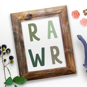 Op de afbeelding: Een ingelijst print met het woord "RAWR" in grote, groene letters. De letters zijn in een verloop van groene tinten. Het frame is van hout en heeft een rustieke uitstraling.