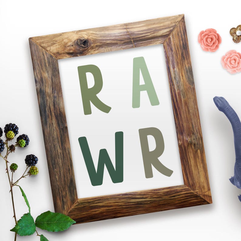 Op de afbeelding: Een ingelijst print met het woord "RAWR" in grote, groene letters. De letters zijn in een verloop van groene tinten. Het frame is van hout en heeft een rustieke uitstraling.