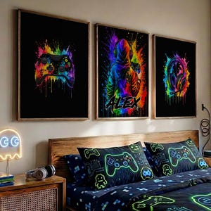 May include: Three framed wall art prints featuring vibrant, multicolored paint splatter designs on black backgrounds. The prints depict a video game controller, a hooded figure with the name ALEX, and gaming headphones, all in a neon color palette.