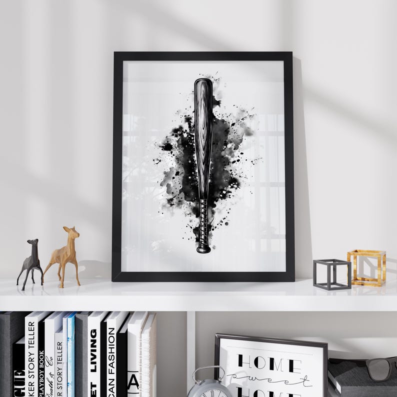 May include: A framed wall art print featuring a black and white watercolor illustration of a baseball bat centered against a dark, splattered ink background. The artwork is enclosed in a simple black frame, showcasing a detailed wood grain texture.