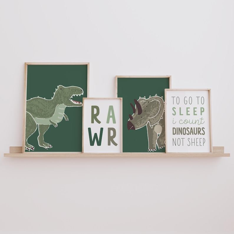 Op de afbeelding: Vier ingelijste prints met een dinosaurus thema. De prints tonen een groene Tyrannosaurus Rex, een groene Triceratops, het woord "RAWR" in groene en bruine letters, en de tekst "TO GO TO SLEEP I COUNT DINOSAURS NOT SHEEP" in groene en bruine letters.