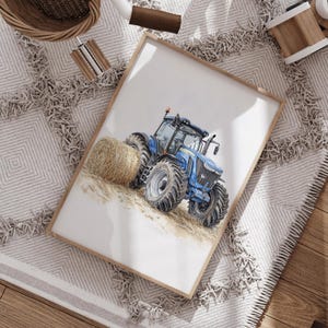 Może przedstawiać: Akwarela przedstawiająca niebieski traktor z dużymi oponami i belą siana. Traktor jest umieszczony na jasnym tle, oprawiony w drewnianą ramę. Grafika znajduje się na białym tle.