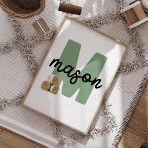 Może przedstawiać: Oprawiony wydruk z imieniem "mason" czcionką skryptową na dużym zielonym "M". Wydruk zawiera małą ilustrację bel siana. Rama jest w jasnym kolorze drewna.