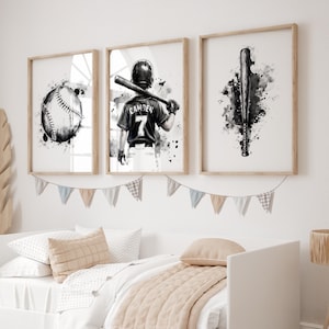 May include: Three framed wall art prints featuring black and white watercolor illustrations of baseball themes. The left print shows a baseball, the center print depicts a player wearing a jersey with the name CAMDEN and number 7, and the right print displays a baseball bat.