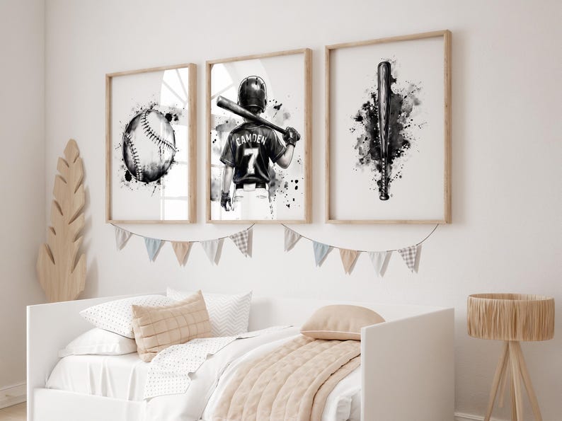 May include: Three framed wall art prints featuring black and white watercolor illustrations of baseball themes. The left print shows a baseball, the center print depicts a player wearing a jersey with the name CAMDEN and number 7, and the right print displays a baseball bat.