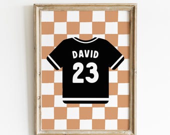 May include: Framed wall art featuring a black jersey with the name "DAVID" and the number "23" in white. The jersey is set against a brown and white checkered background, all within a wooden frame.
