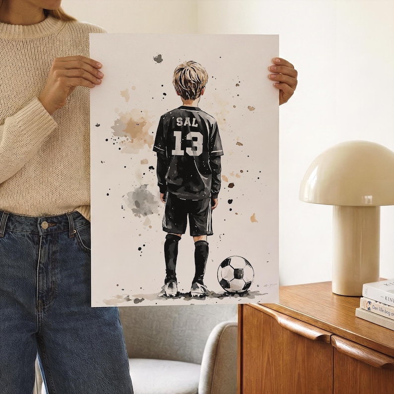 Puede incluir: Una l&aacute;mina art&iacute;stica estilo acuarela que muestra a un ni&ntilde;o visto desde atr&aacute;s, con una camiseta de f&uacute;tbol negra con el nombre SAL y el n&uacute;mero 13 impresos en blanco. El ni&ntilde;o lleva pantalones cortos y calcetines negros junto a un bal&oacute;n.