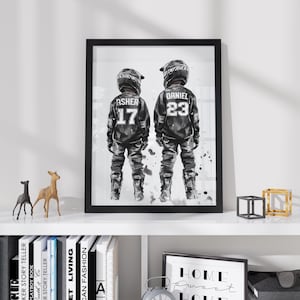 May include: A framed black and white art print featuring two motocross riders standing side by side. The left rider wears a jersey with the name ASHER and number 17, while the right rider wears a jersey with the name DANIEL and number 23.