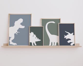 May include: Four framed prints of dinosaur silhouettes on a wooden shelf. The prints are in shades of blue and green, with white dinosaur silhouettes. The dinosaurs include a Tyrannosaurus Rex, a Brachiosaurus, a Stegosaurus, and a Triceratops.