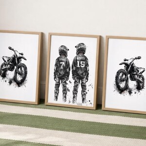 May include: Three framed wall art prints with light wood frames. Two prints feature black and white watercolor-style illustrations of dirt bikes. The center print shows two individuals in motocross gear with the names Davis 7 and Asher 15.