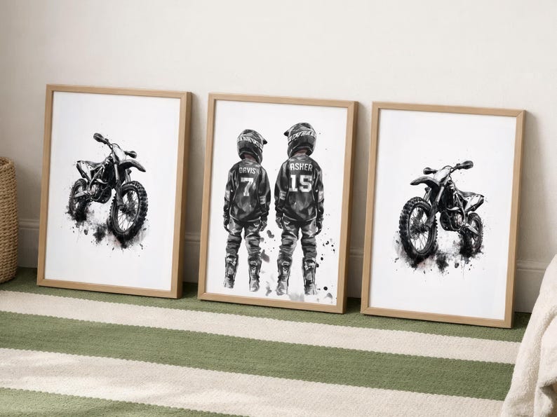 May include: Three framed wall art prints with light wood frames. Two prints feature black and white watercolor-style illustrations of dirt bikes. The center print shows two individuals in motocross gear with the names Davis 7 and Asher 15.