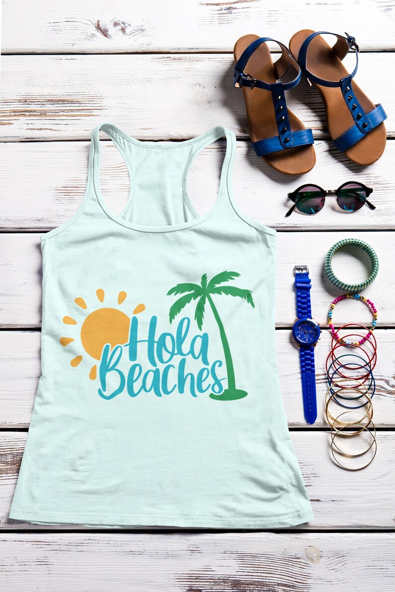 K&ouml;nnte beinhalten: Ein hellblaues Tanktop mit einem Palmen- und Sonnenmotiv und dem Text "Hola Beaches". Das Tanktop liegt flach auf einer wei&szlig;en Holzoberfl&auml;che mit einem Paar blauer Sandalen, einer Sonnenbrille, einer blauen Uhr und mehreren Armb&auml;ndern.