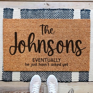 May include: A brown coir doormat with the text "The Johnsons Eventually he just hasn't asked yet" in black lettering.