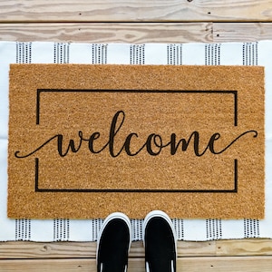May include: A brown welcome mat with white fringe and the word "welcome" in a black cursive font.