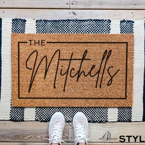May include: A brown coir doormat with the text "THE Mitchells" in black lettering on a white background.