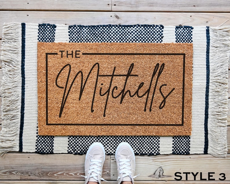 May include: A brown coir doormat with the text "THE Mitchells" in black lettering on a white background.