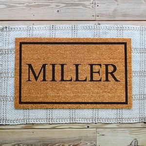 A coir doormat that has a customizable name, number, or initial in the center surrounded by a border.