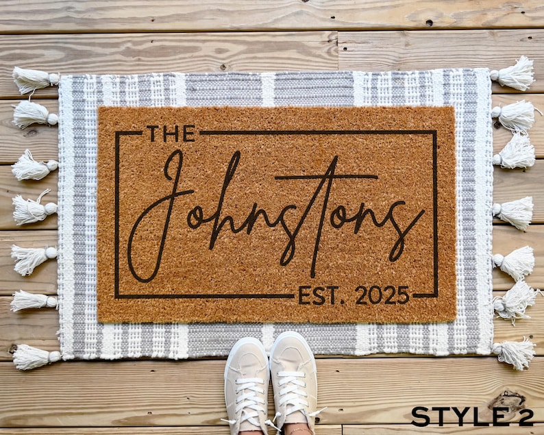 May include: A brown coir doormat with white fringe. The doormat has a black frame with the text "The Johnstons Est. 2025" printed on it.