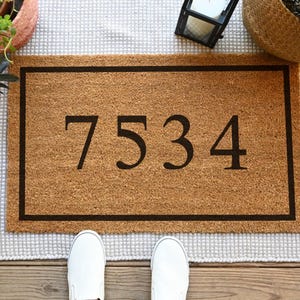 A coir doormat that has a customizable name, number, or initial in the center surrounded by a border.