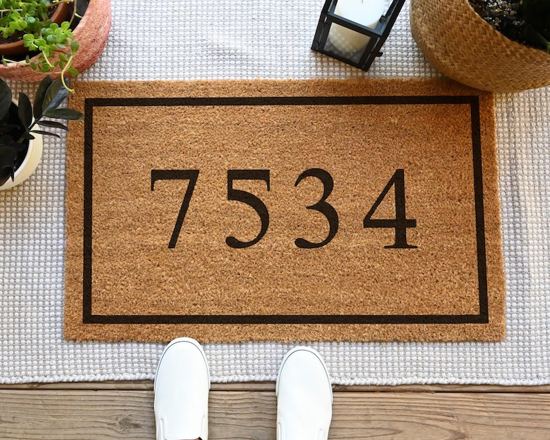 A coir doormat that has a customizable name, number, or initial in the center surrounded by a border.