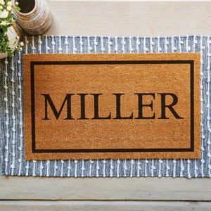 A coir doormat that has a customizable name, number, or initial in the center surrounded by a border.