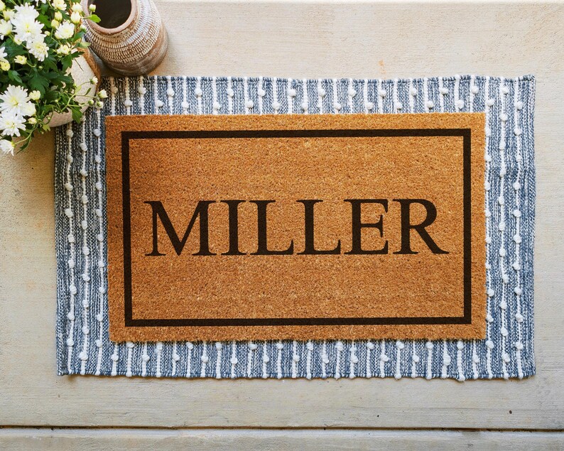 A coir doormat that has a customizable name, number, or initial in the center surrounded by a border.