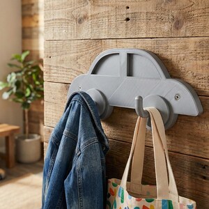 Könnte beinhalten: Ein grauer, auto-förmiger Wandhaken mit einer Jeansjacke und einer Tragetasche, die daran hängen. Der Haken ist an einer Holzwand befestigt. Ein kleines Spielzeugauto liegt auf dem Boden.