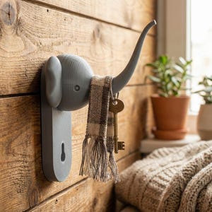 Peut inclure: Un crochet mural gris en forme d'éléphant en plastique, monté sur un mur en bois. Le crochet tient une écharpe et deux clés. La trompe de l'éléphant se courbe vers le haut pour former le crochet. Le mur est fait de planches de bois horizontales.