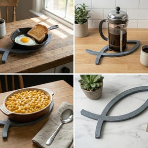 Könnte beinhalten: Grauer, 3D-gedruckter Ichthus-Topfuntersetzer. Der Topfuntersetzer hat die Form eines Fisches und wird mit einer gusseisernen Pfanne mit Ei und Toast, einer French Press und einer Auflaufform gezeigt. Der Topfuntersetzer ist etwa 23 cm lang.