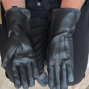 May include: A pair of black leather gloves. The gloves have a smooth texture and a classic design, with a long cuff and detailed stitching. The gloves are shown from a top-down perspective.