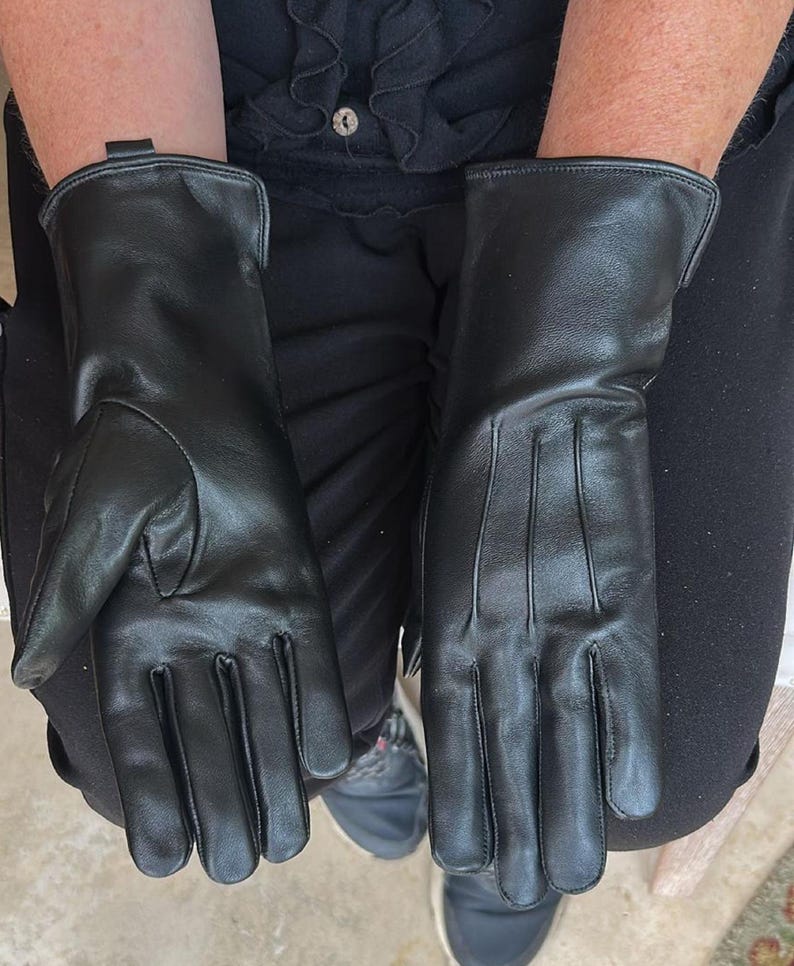 May include: A pair of black leather gloves. The gloves have a smooth texture and a classic design, with a long cuff and detailed stitching. The gloves are shown from a top-down perspective.
