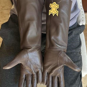 May include: A pair of brown leather gloves with long gauntlets. The gloves have a tag that reads "Genuine Leather". The gloves are designed to protect the hands and forearms.