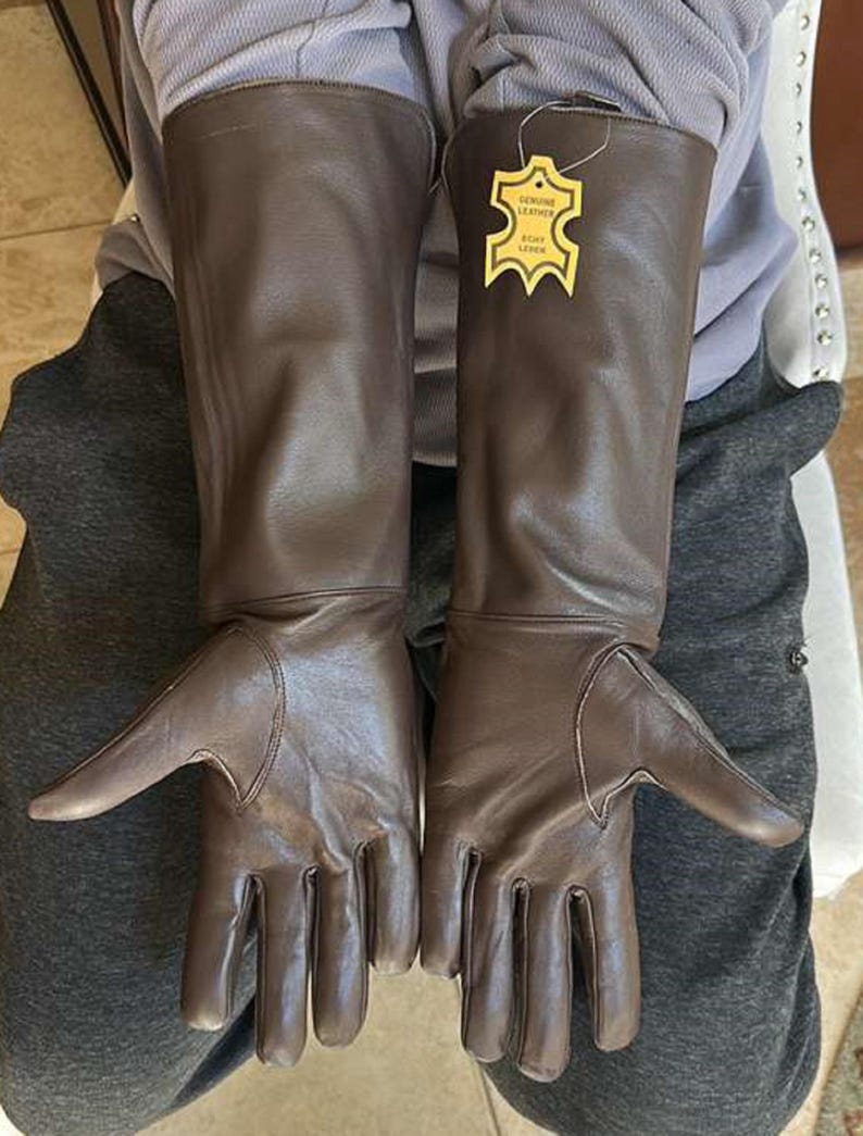 May include: A pair of brown leather gloves with long gauntlets. The gloves have a tag that reads "Genuine Leather". The gloves are designed to protect the hands and forearms.