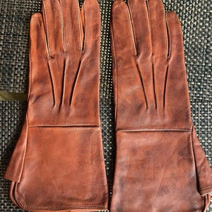 May include: A pair of brown leather gloves with a long cuff. The gloves have a classic design with visible stitching and are made of a smooth, supple leather. The gloves are a warm, reddish-brown color.