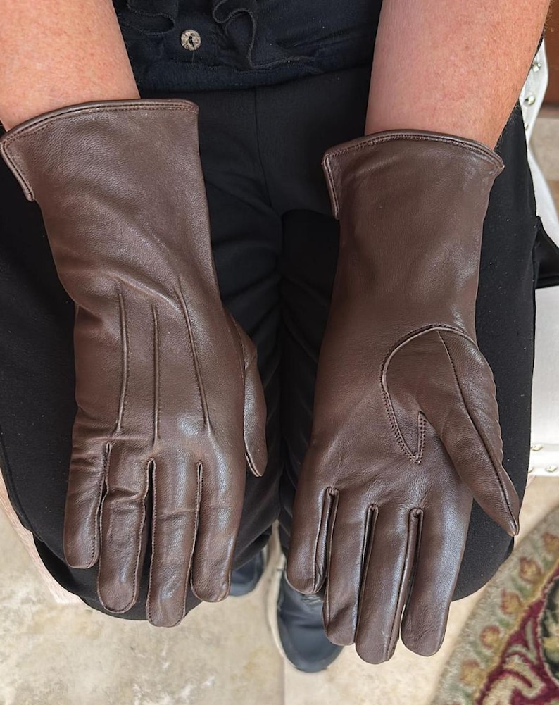 May include: A pair of brown leather gloves. The gloves are a rich, dark brown color and appear to be made of soft leather. The gloves have a classic design with a smooth finish and are likely designed for warmth and protection.