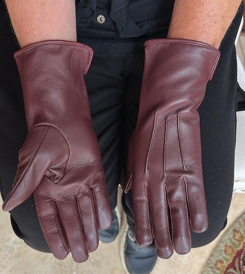 May include: A pair of burgundy leather gloves. The gloves are a deep red-purple color, with a smooth texture and visible stitching details. The gloves have a classic design, with a long cuff.